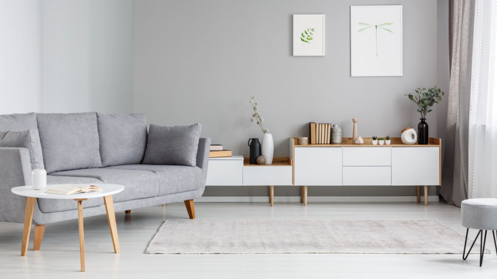 Grey settee near white cupboard in minimal living room interior with posters on the wall.