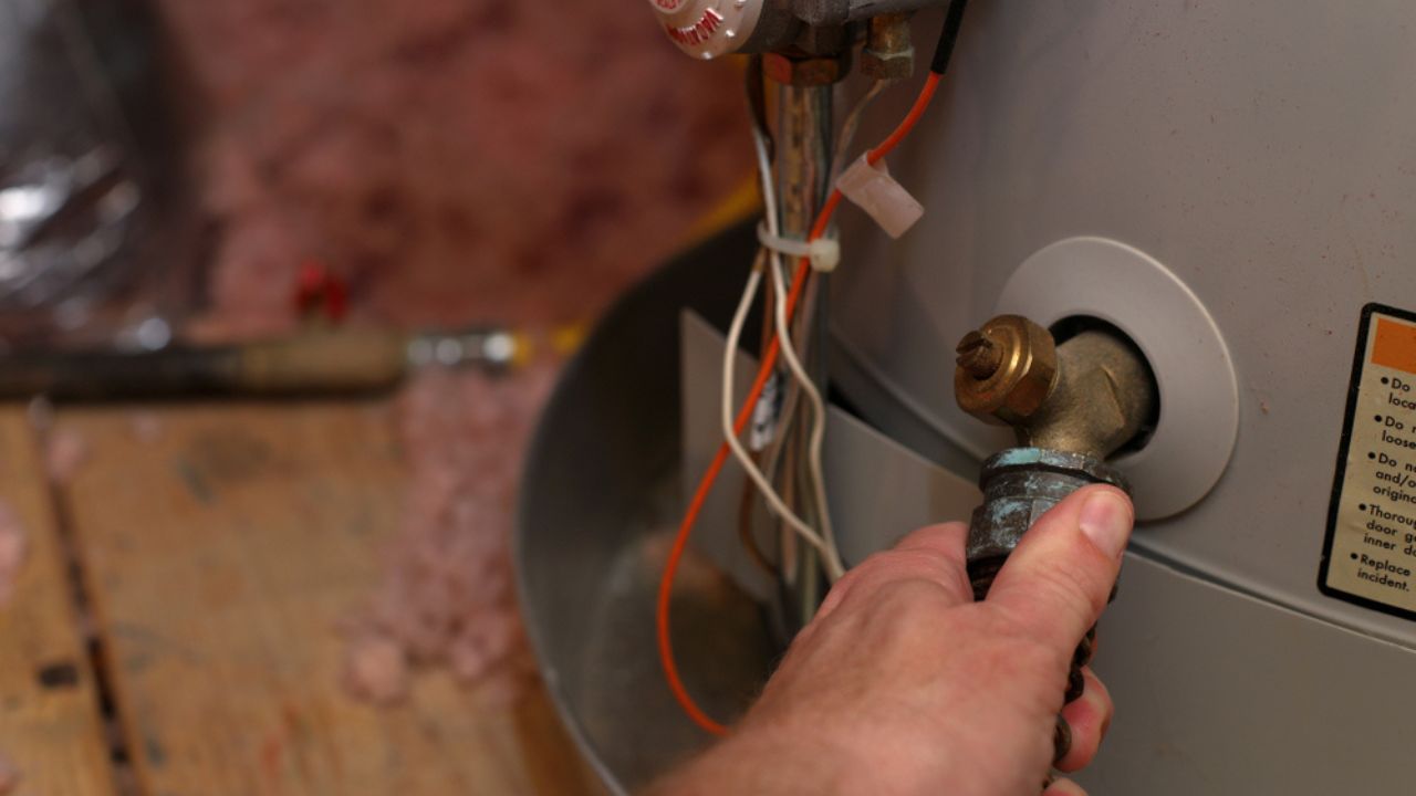 Hand attaches hose to water heater drain to perform maintenance
