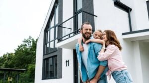 Happy bearded man piggybacking daughter near cheerful wife and home
