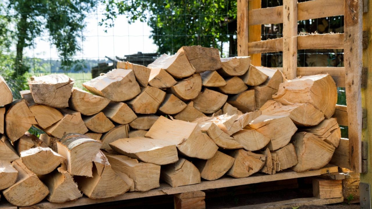 Pile of firewood in the summer stocked outdoors in a shed, being prepared for winter