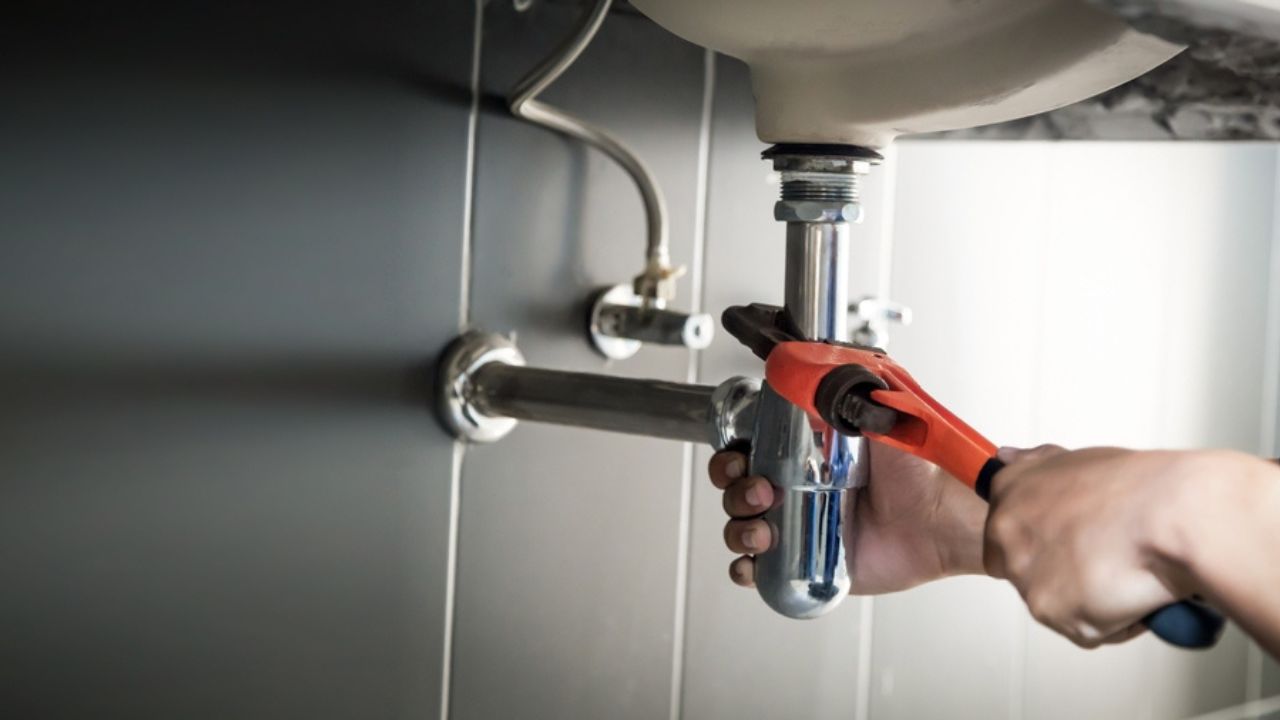 Plumber uses wrench to repair water pipe under sink There is maintenance to fix the water leak in the bathroom.with red wrench, plumbing install concept.