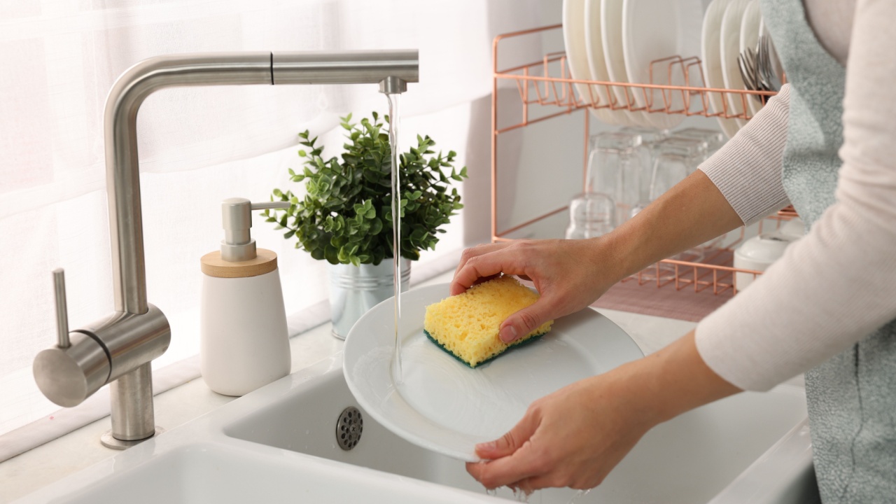 Woman washing plate with sponge at sink in kitchen, closeup