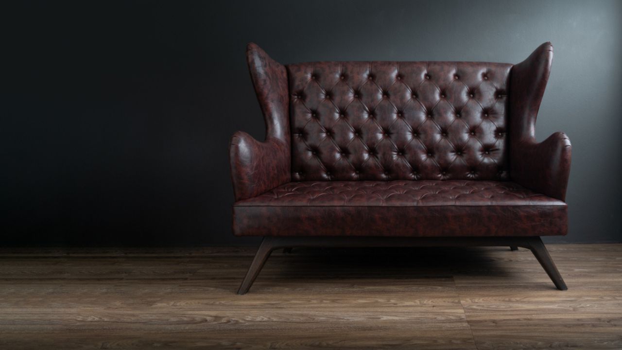 Sofa of black leather standing in center on concrete floor against dark grey wall with copy space. Vintage brown leather sofa with grunge gray wall living room.