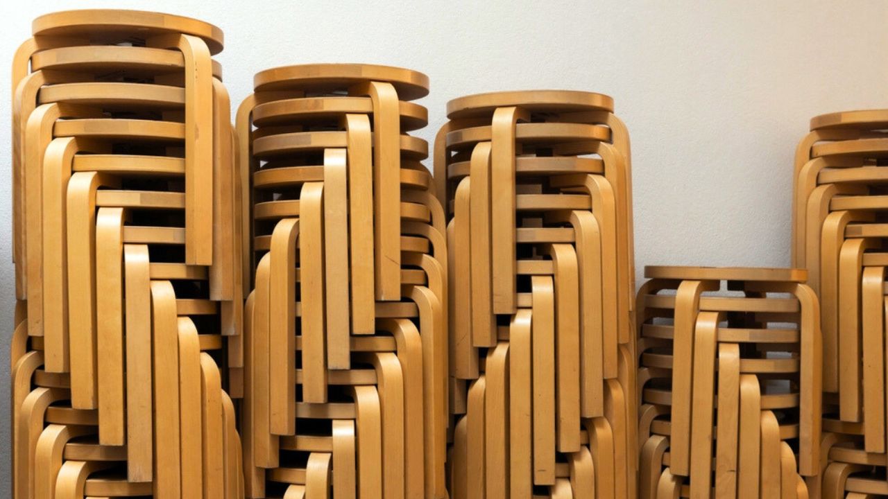 Stacked vintage wooden stools made from bent plywood stand in front of a white wall