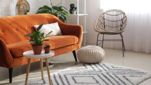 Stylish orange sofa with houseplants in modern interior of living room with round carpet