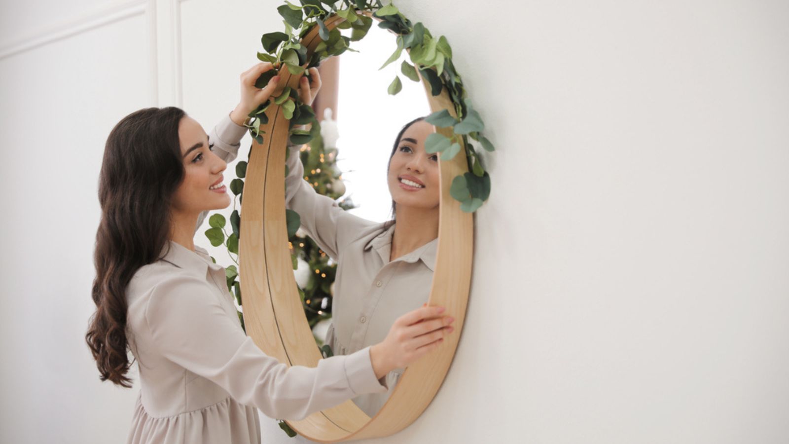 Woman decorating mirror with eucalyptus branches at home