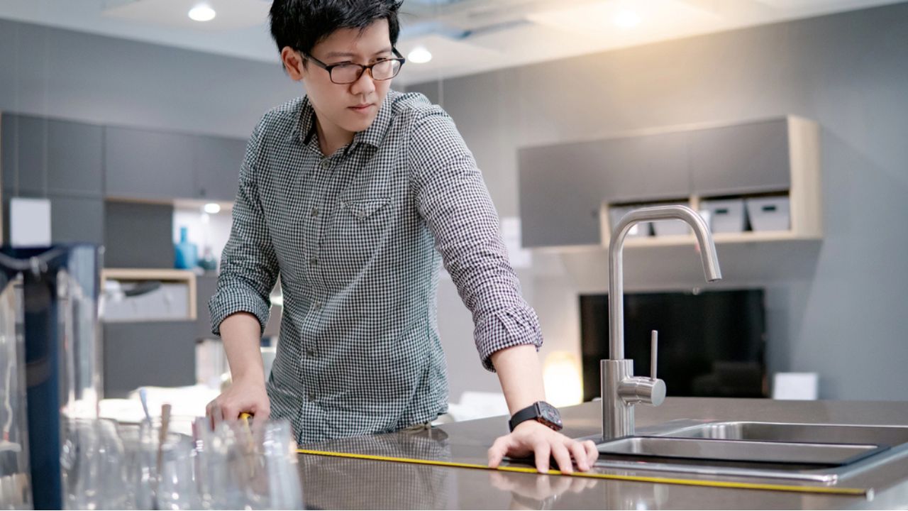 Young Asian man using tape measure for measuring granite countertops on modern kitchen counter in showroom. Shopping furniture for home improvement. Interior design concept