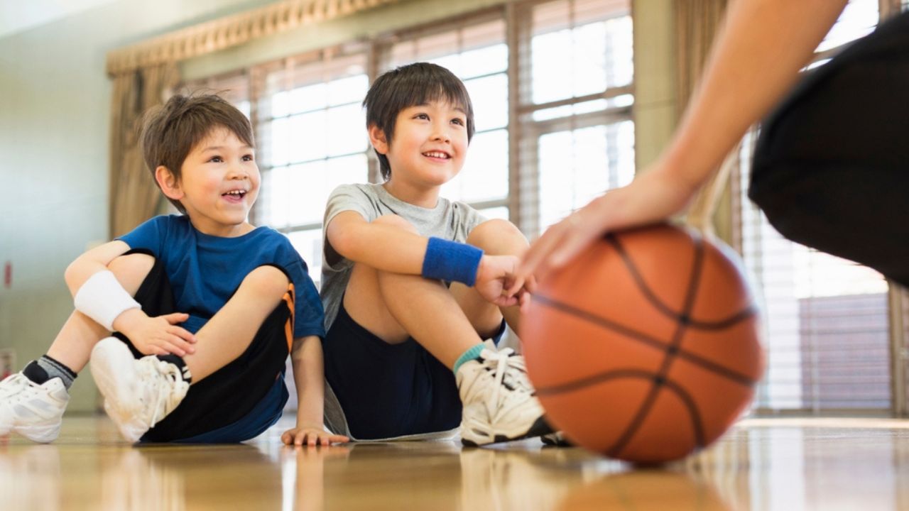 Young boys practising on a basketball court with a young male coach.