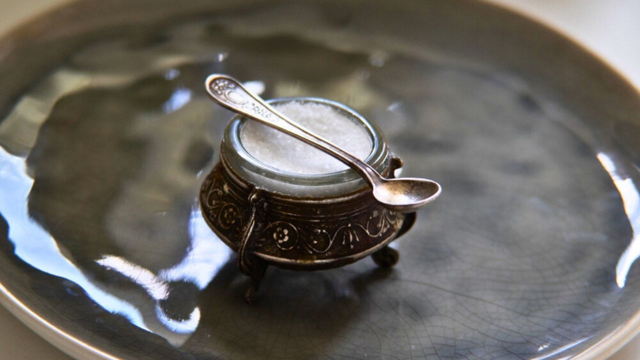 A close-up of a vintage silver salt cellar with a delicate miniature spoon placed on a ceramic plate with a unique texture.