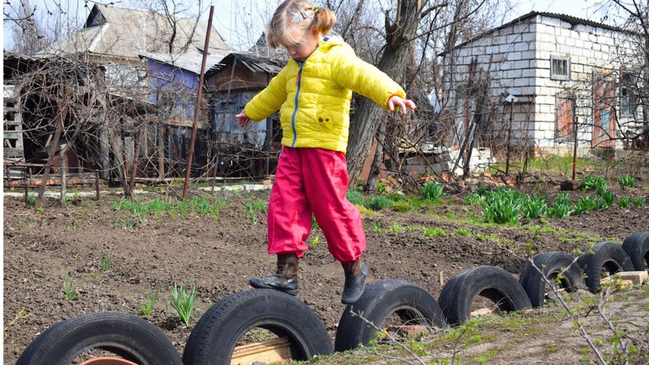 A girl walks on tires while maintaining her balance in the backyard.