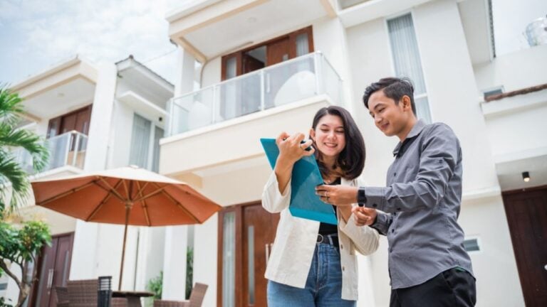 Asian female real estate agent showing clipboard chatting with man in residential background