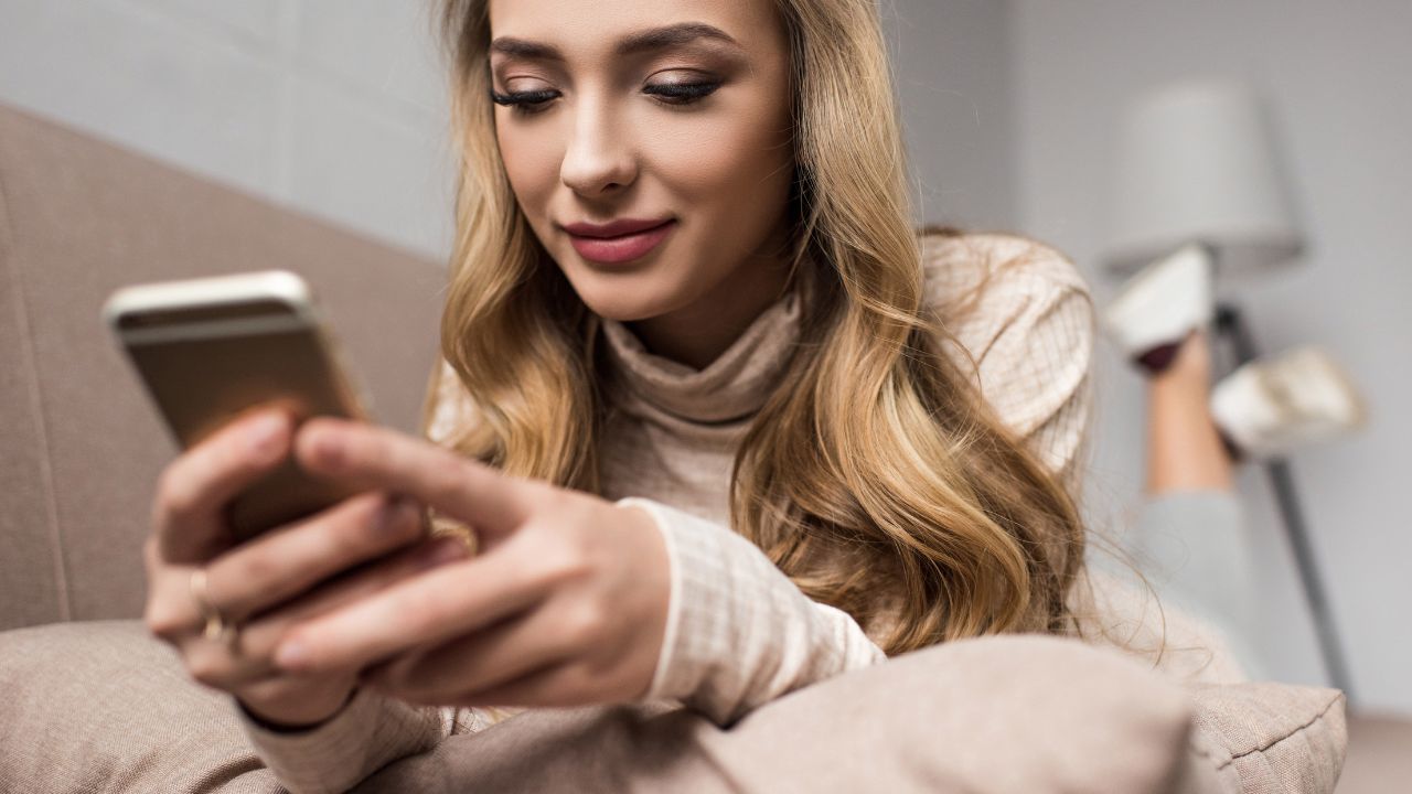 Attractive young woman using smartphone while lying on couch at home