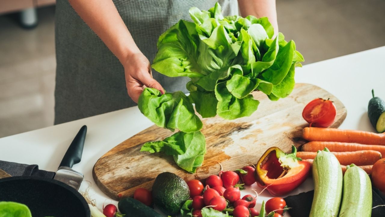 Close Up Photo of Woman Hands Making Fresh Salad on a Table Full with Organic Vegetables. An anonymous housewife making lunch with fresh colorful vegetables at kitchen table.