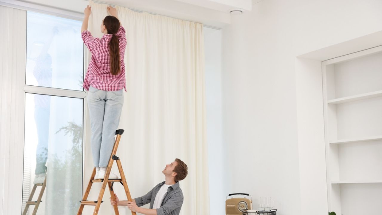 Couple putting up curtains using ladder in room