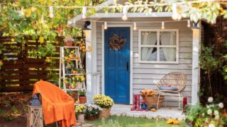 Cozy wooden house porch with chair, blanket, potted chrysanthemums and pumpkins. Decor outdoor of autumn yard. Facade House decorated for autumn holidays.