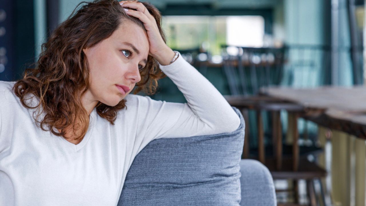 Depressed young woman feeling down on a day alone at home. She is sitting at home in the living room on the couch and thinking
