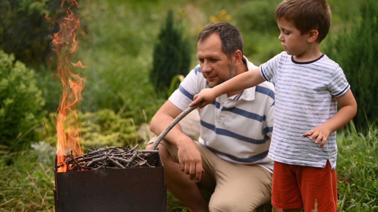 Father and son making fire outdoors. Fire safety. Forest fire. Time with kids, outdoor recreation, barbecue picnic. Father's Day