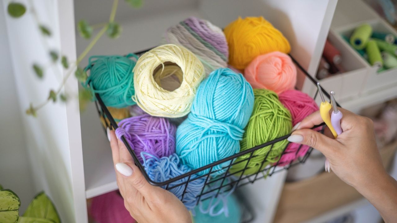Female hands placing basket with colored ball of yarn for art crochet knitting ribbon cotton wool thread for hobby. Woman tailor sewing materials