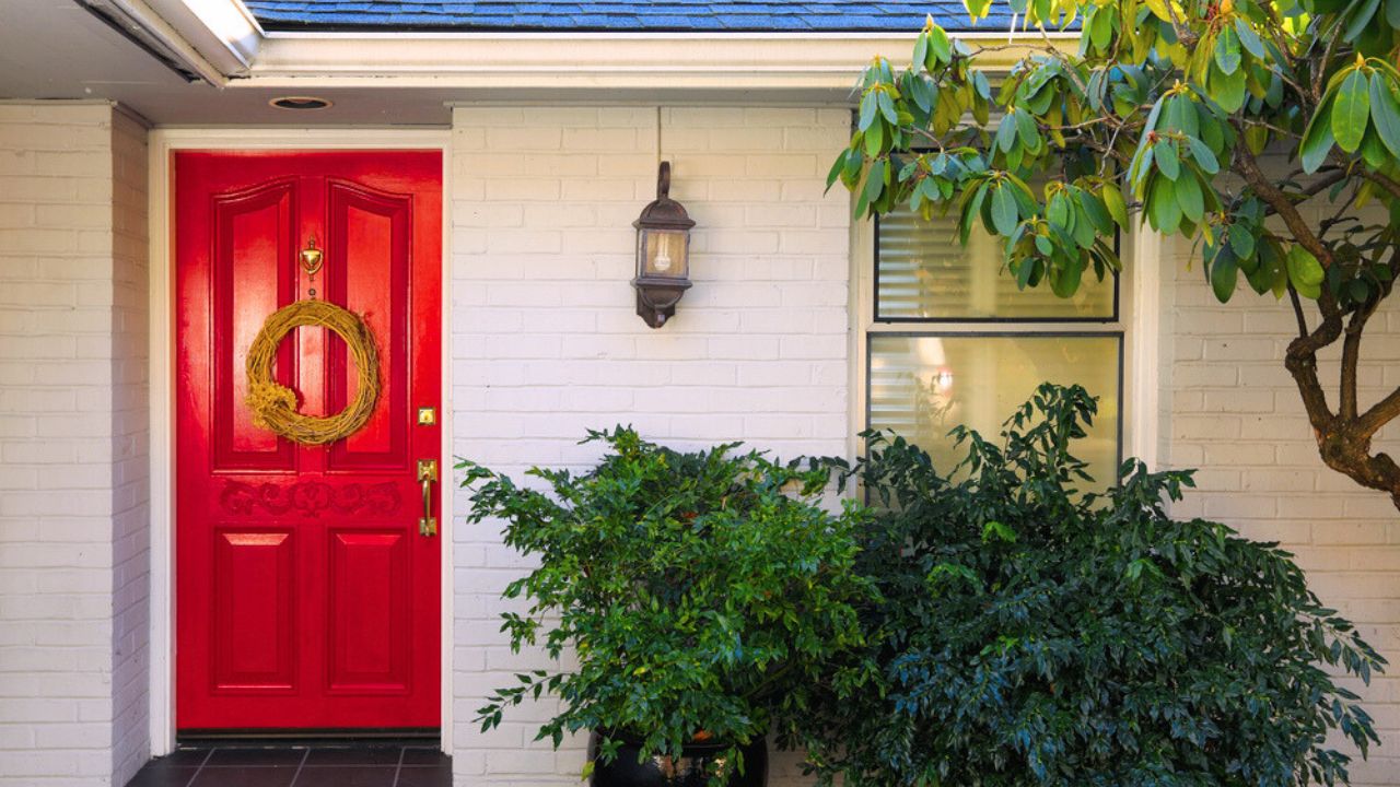 Front porch with white painted brick exterior, red entrance door accented with Door Wreath and finished with pot planter under wall lantern. Northwest, USA