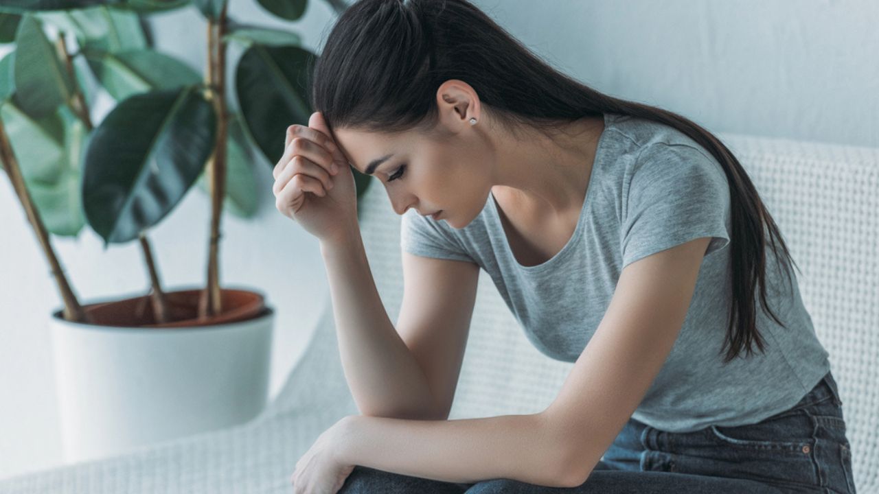 Frustrated young woman in depression sitting on couch and looking down