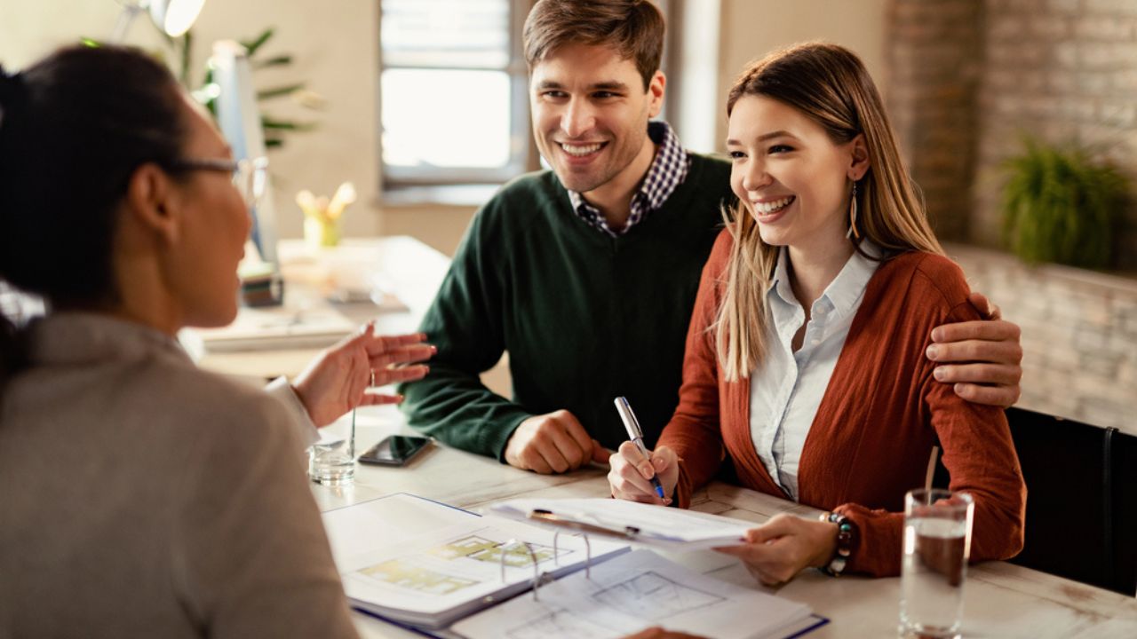 Happy Couple Signing Mortgage Contract While Having Meeting with Real Estate Agent.