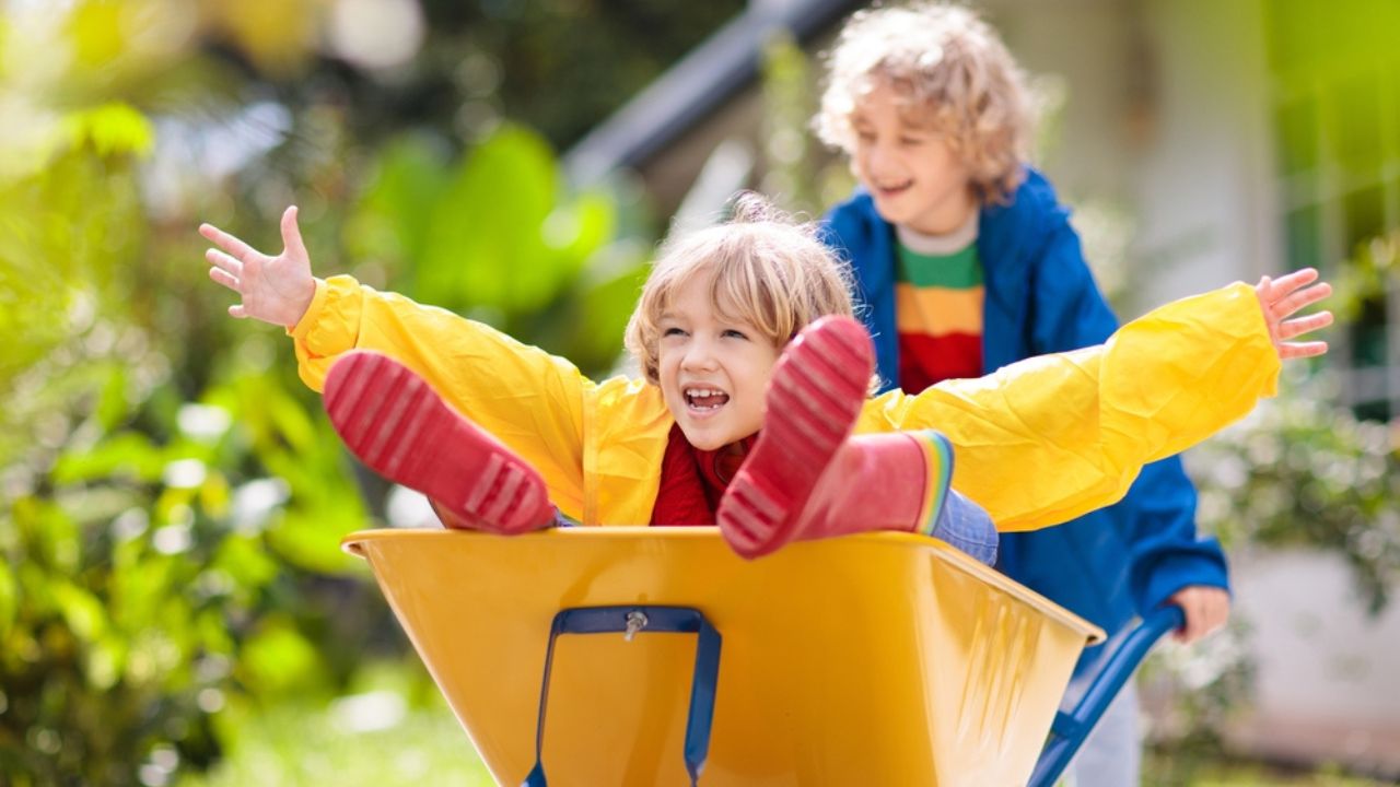 Kids in wheelbarrow on pumpkin patch. Autumn outdoor fun for children in Thanksgiving and Halloween season.