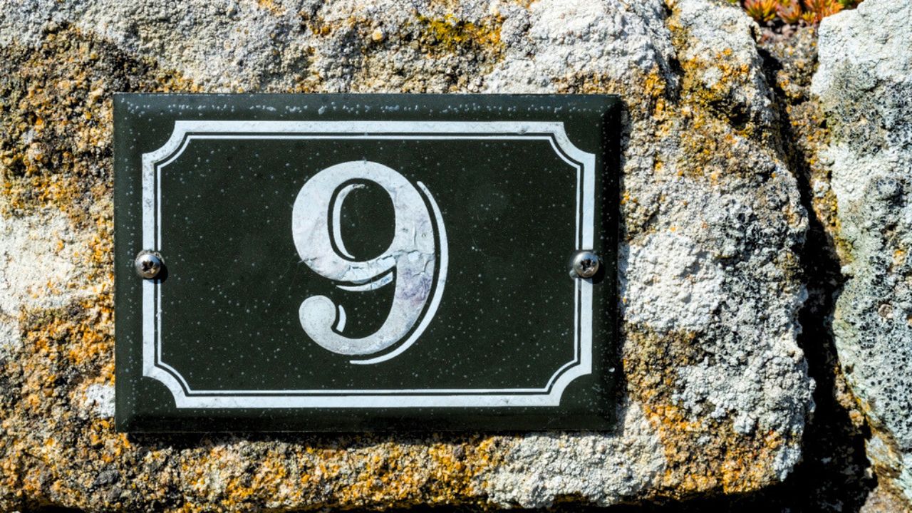 Modern house number nine, metal plate on textured wall
