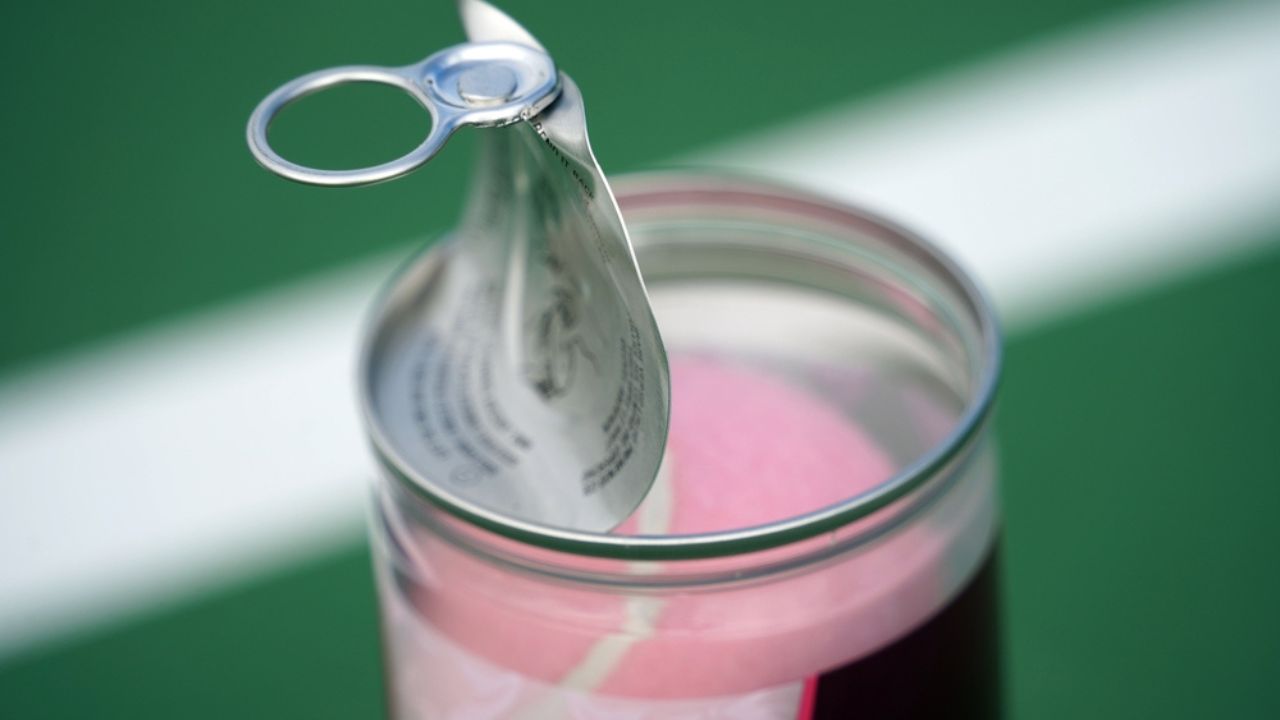 Opening a can of tennis balls with tennis court in background.