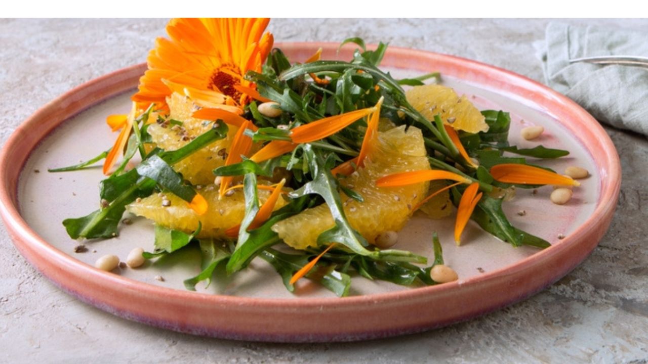 Plate with salad with arugula, oranges and edible calendula flowers on a light table