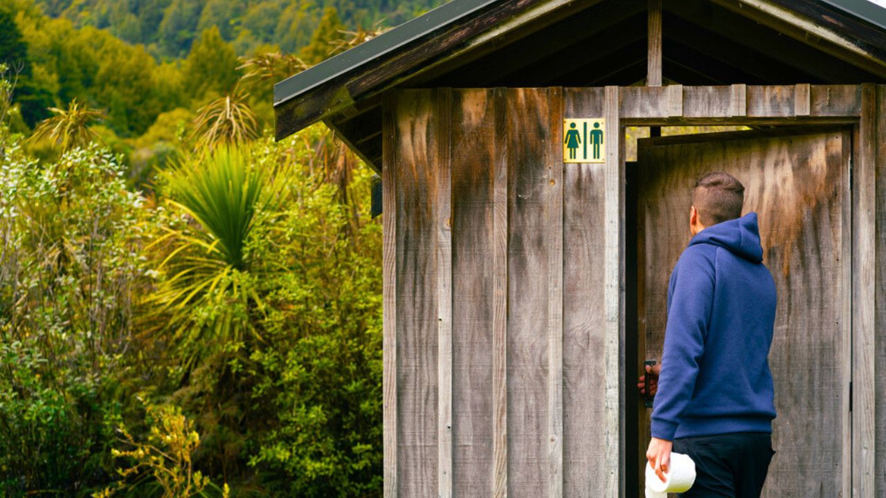 Public toilet in the forest and a person going into it with toilet paper in hand. Selective focus