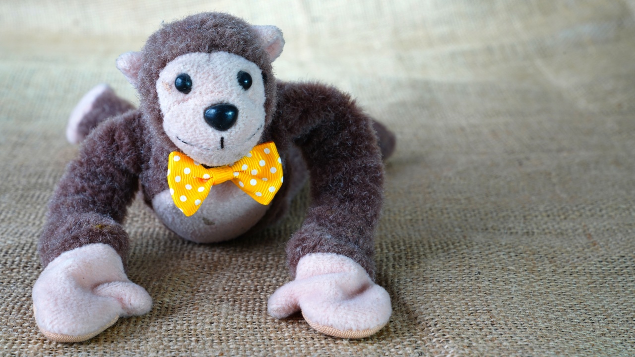Cute soft toy monkey with yellow bow tie lying on floor
