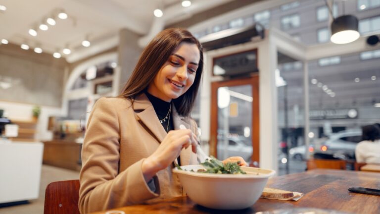 Girl eats vegetable salad. Lady sitting in a cafe. Brunette in a brown coat