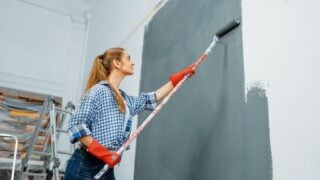 Female house painter in gloves paints the wall