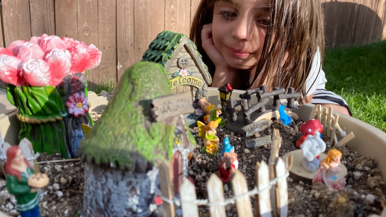 A little girl looking fondly at a gardening gnome village she made in an empty flower pot.