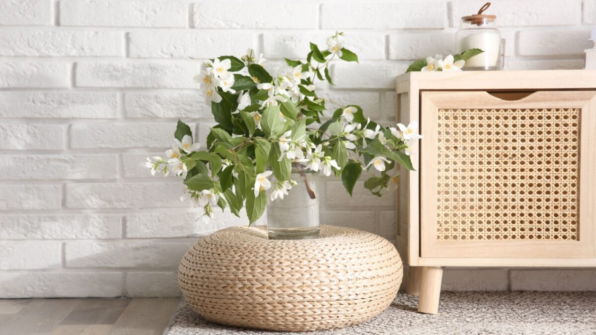 Bouquet of beautiful jasmine flowers in glass vase near white brick wall indoors