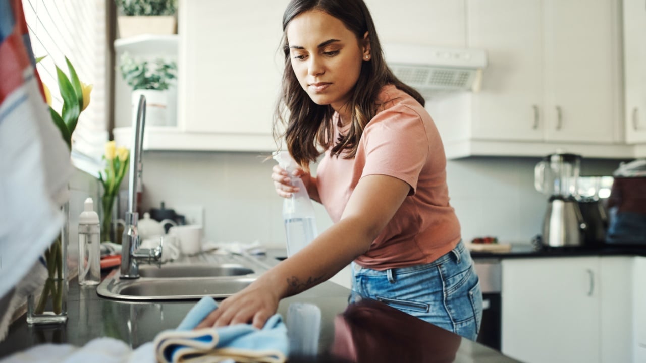 Keeping these countertops clean is a full time job. Shot of an attractive young woman using a cloth to clean the kitchen counters at home.