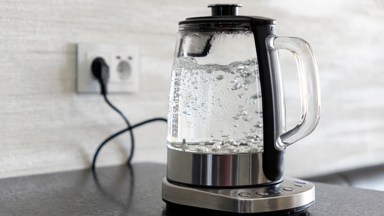 Transparent electric kettle with boiling water on table in the kitchen