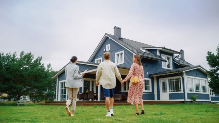 Real Estate Agent Showing a Beautiful Big House to a Young Successful Couple. People Standing Outside on a Warm Day on a Lawn, Talking with Businesswoman, Discussing Buying a New Home.