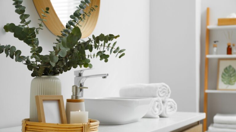 Vase with eucalyptus branches and toiletries near vessel sink in bathroom, space for text. Interior design