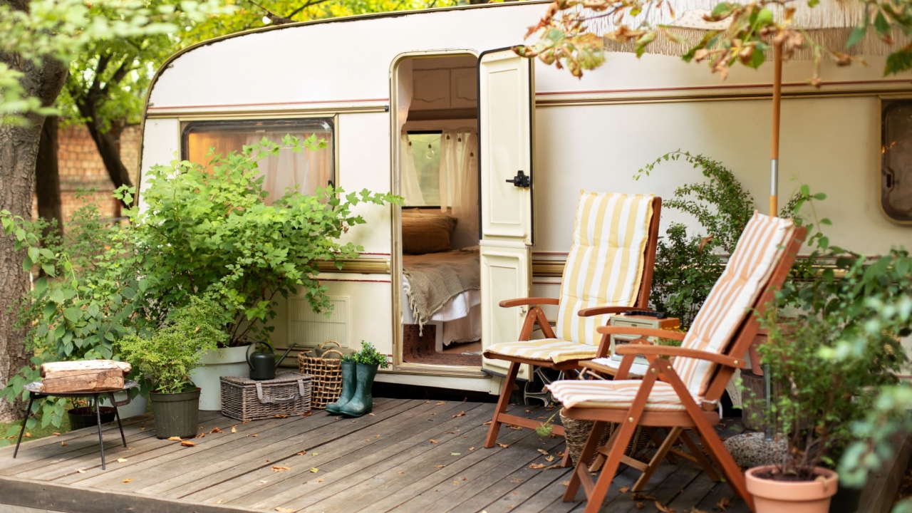 Trailer of mobile home stands in garden in camping. Backyard with RV house with garden furniture. Two deckchairs near outside caravan trailer