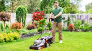 Middle aged man houseowner mowing the lawn on backyard of his house, making beautiful landscape design