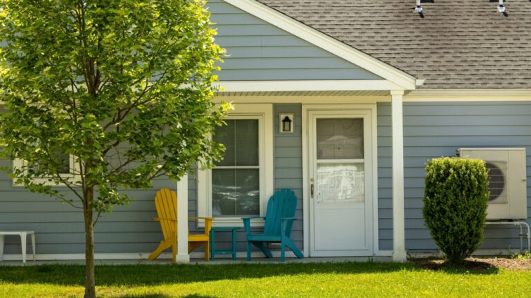 A quaint suburban home with a blue and yellow Adirondack chairs on the front porch.