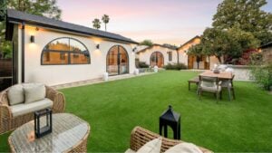 Modern backyard with lush green lawn, wicker furniture, and elegant lighting at sunset.