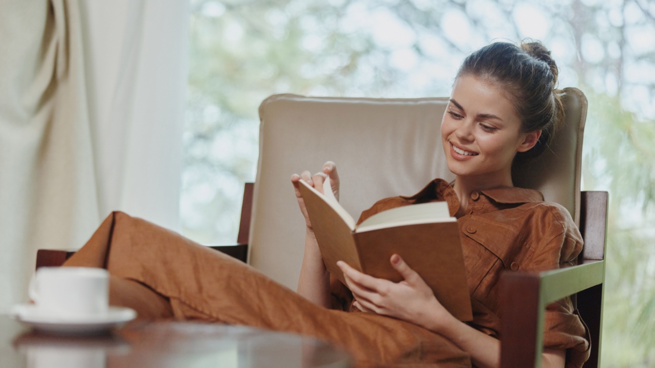 Relaxed woman enjoying a book in a cozy living room, dressed in a brown outfit, showcasing a serene expression against a soft