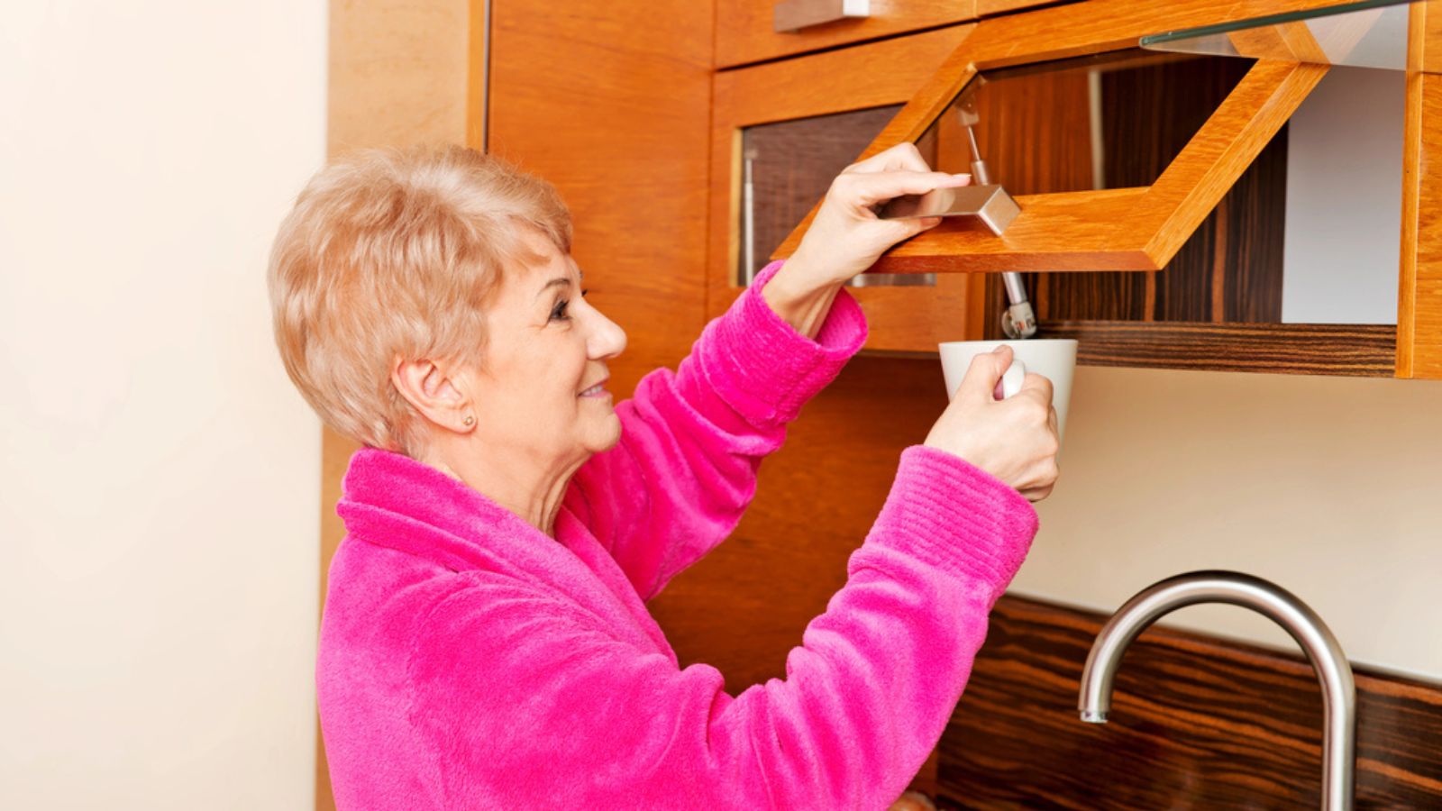 Smile senior woman taking mug from a kitchen cabinet