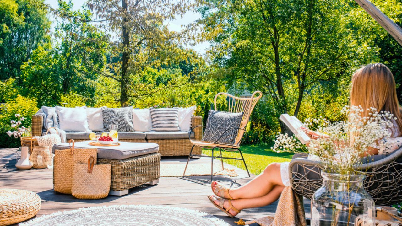 Woman reading book while relaxing at terrace with rattan furniture in the garden. Real photo