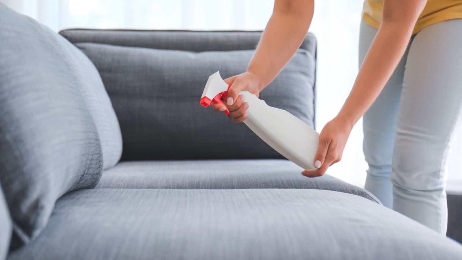 Woman spraying to sofa at home