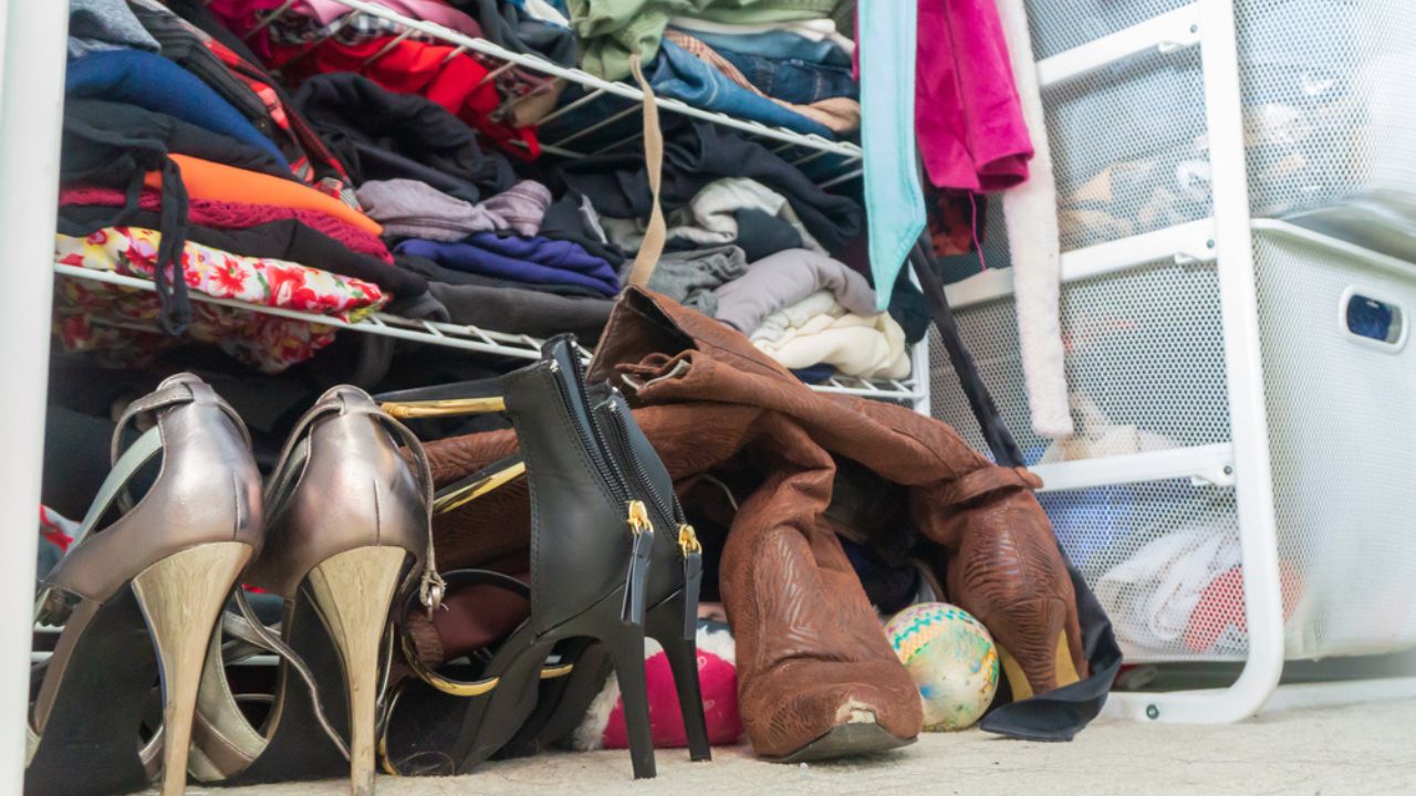 Woman's closet with high heel shoes, stacked, folded clothes on shelves and part of robes hanging. Depicting closet organization, time to donate clothes, fashion lifestyle, consumerism, etc.