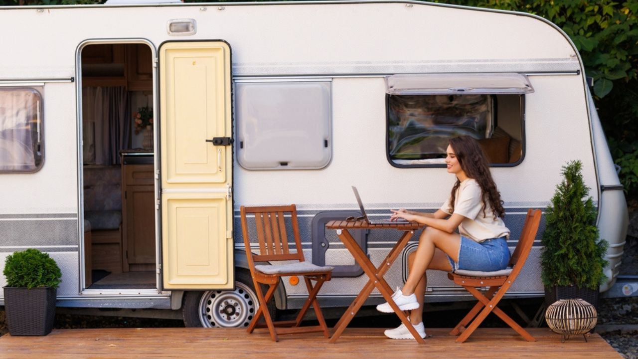 Young pretty woman sitting at tabler with laptop in front of camper