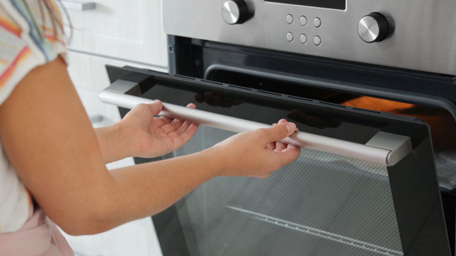 Young woman opening electric oven in kitchen, closeup